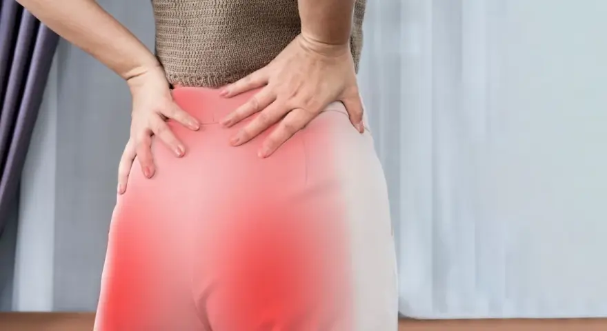 Kobieta trzyma się za bolące biodra i dolną część pleców, gdzie widoczne są czerwone plamy. To mogą być objawy korzonków.