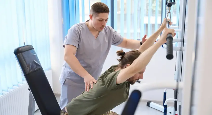 Fizjoterapeuta pomaga pacjentowi ćwiczyć na ławce rehabilitacyjnej z użyciem wyciągu.